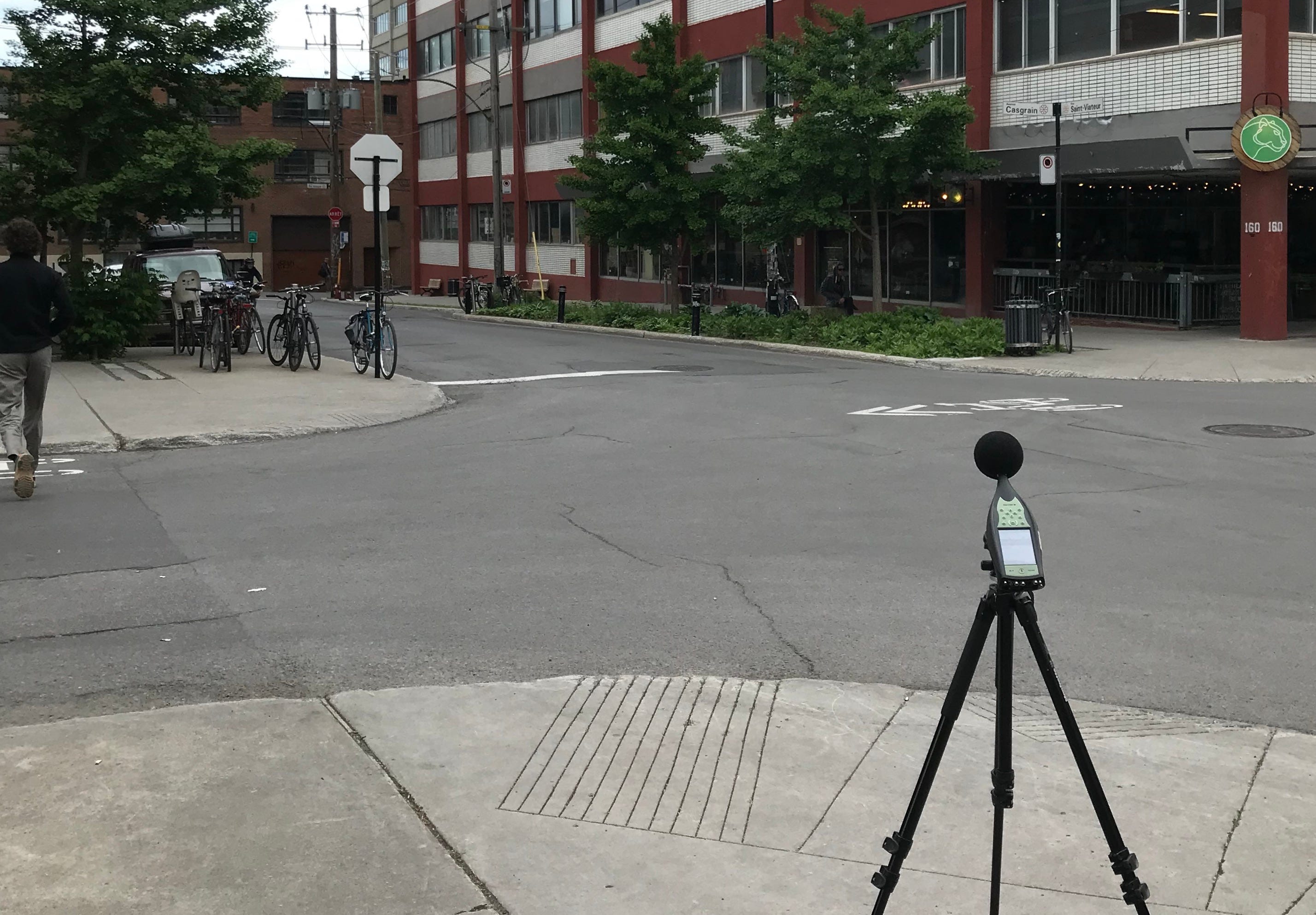 On voit un trépied sur lequel est fixé un sonomètre, installé sur le trottoir à l'angle des rues Saint-Viateur et Casgrain.