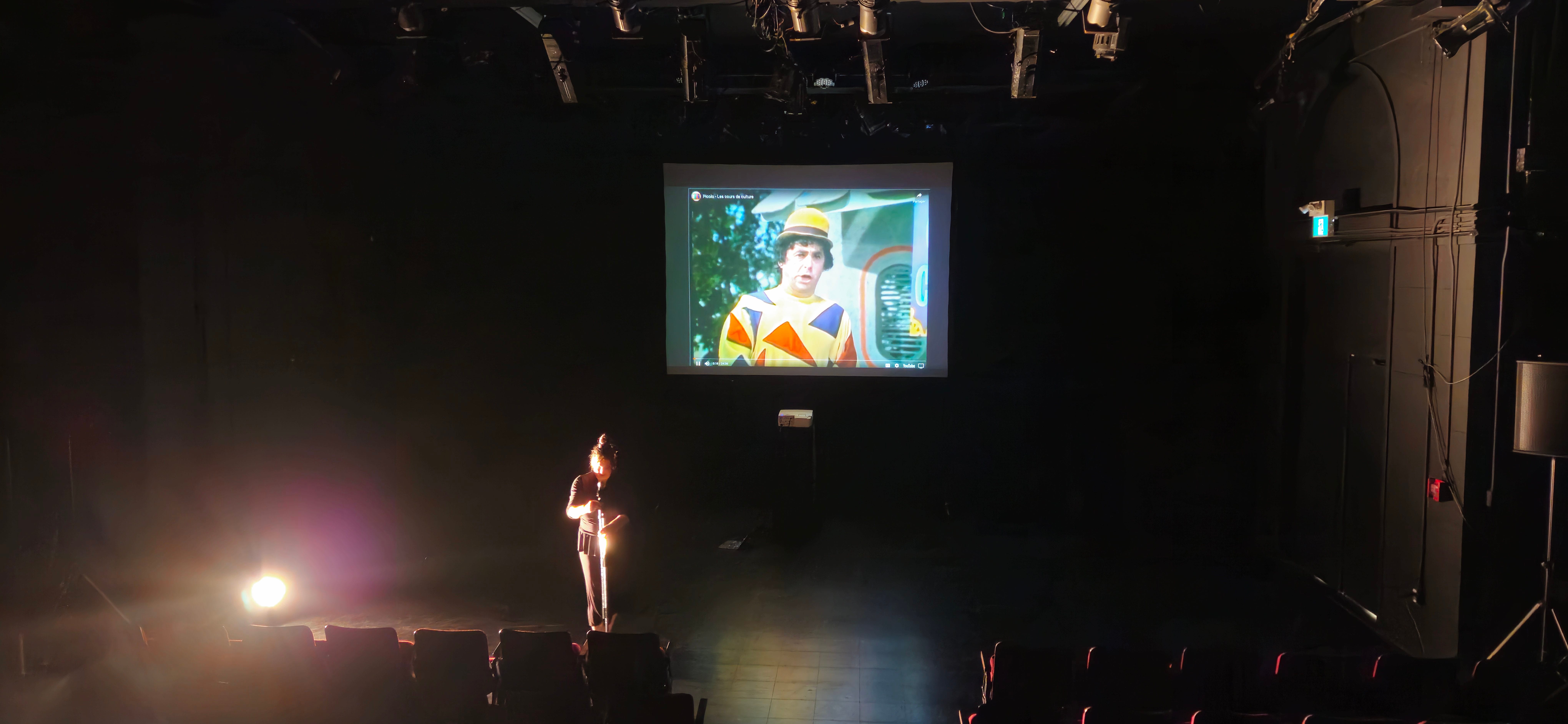 On voit la scène de la salle Paul-Buissonneau avec une projection et une femme devant un micro.