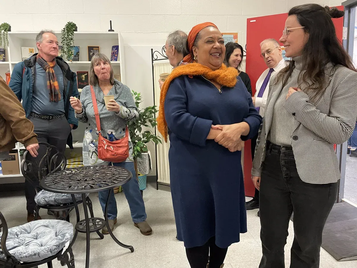 Le photo présente l'entrée du local, avec plusieurs personnes qui parlent et mangent.