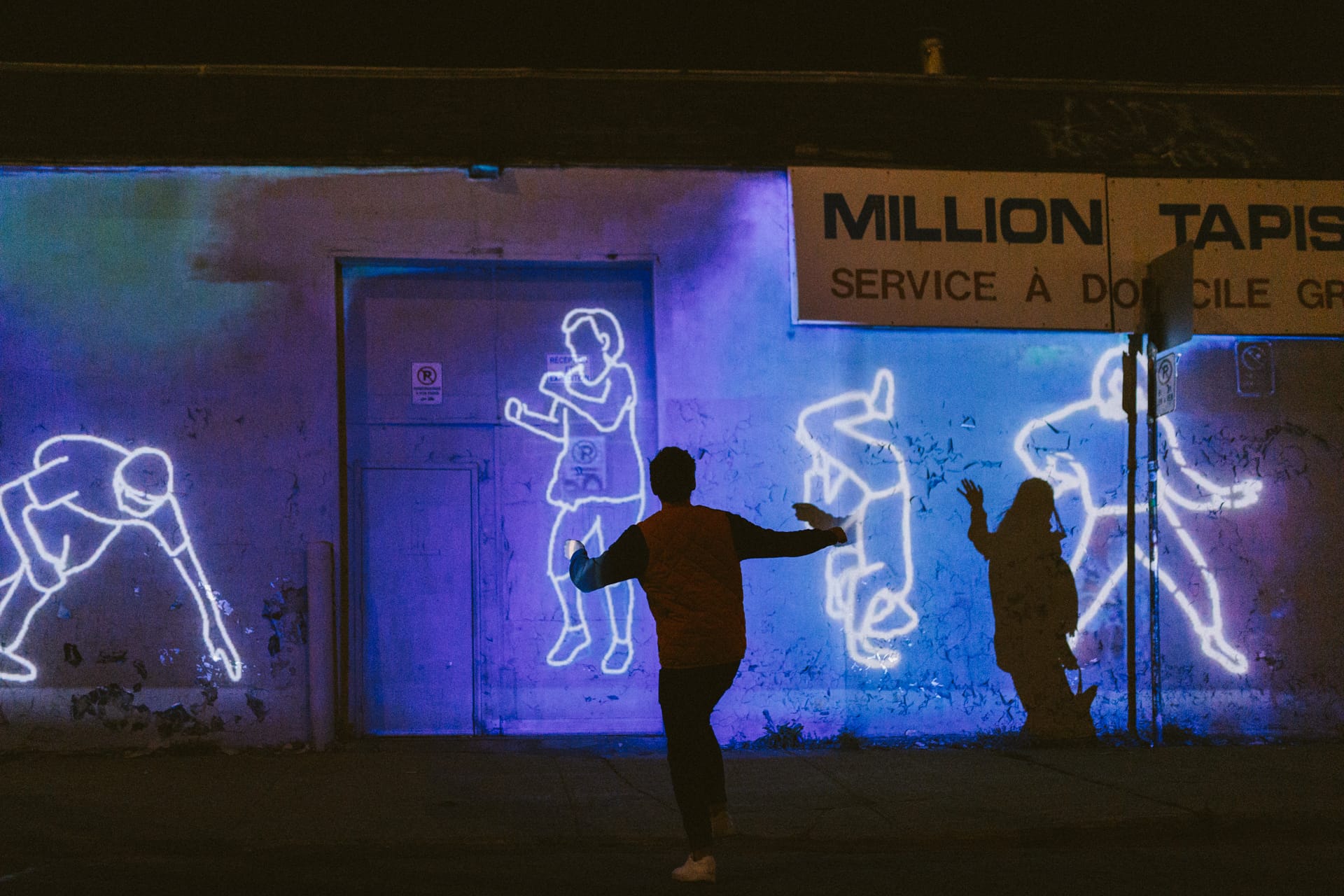 Un homme semble danser devant les projections de corps sur un mur.