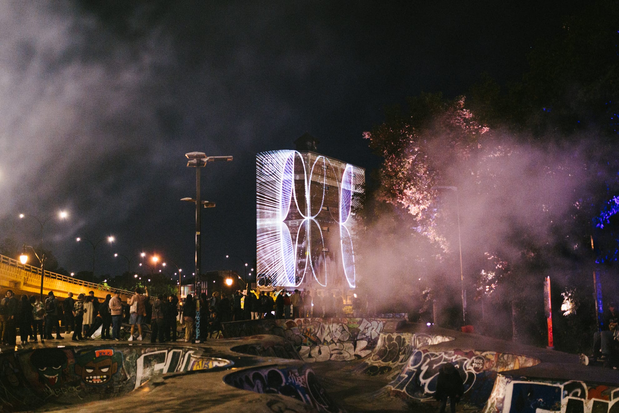 Une petite foule dans un planchodrôme du Mile End regarde les projections sur l'entrepôt Van Horne.