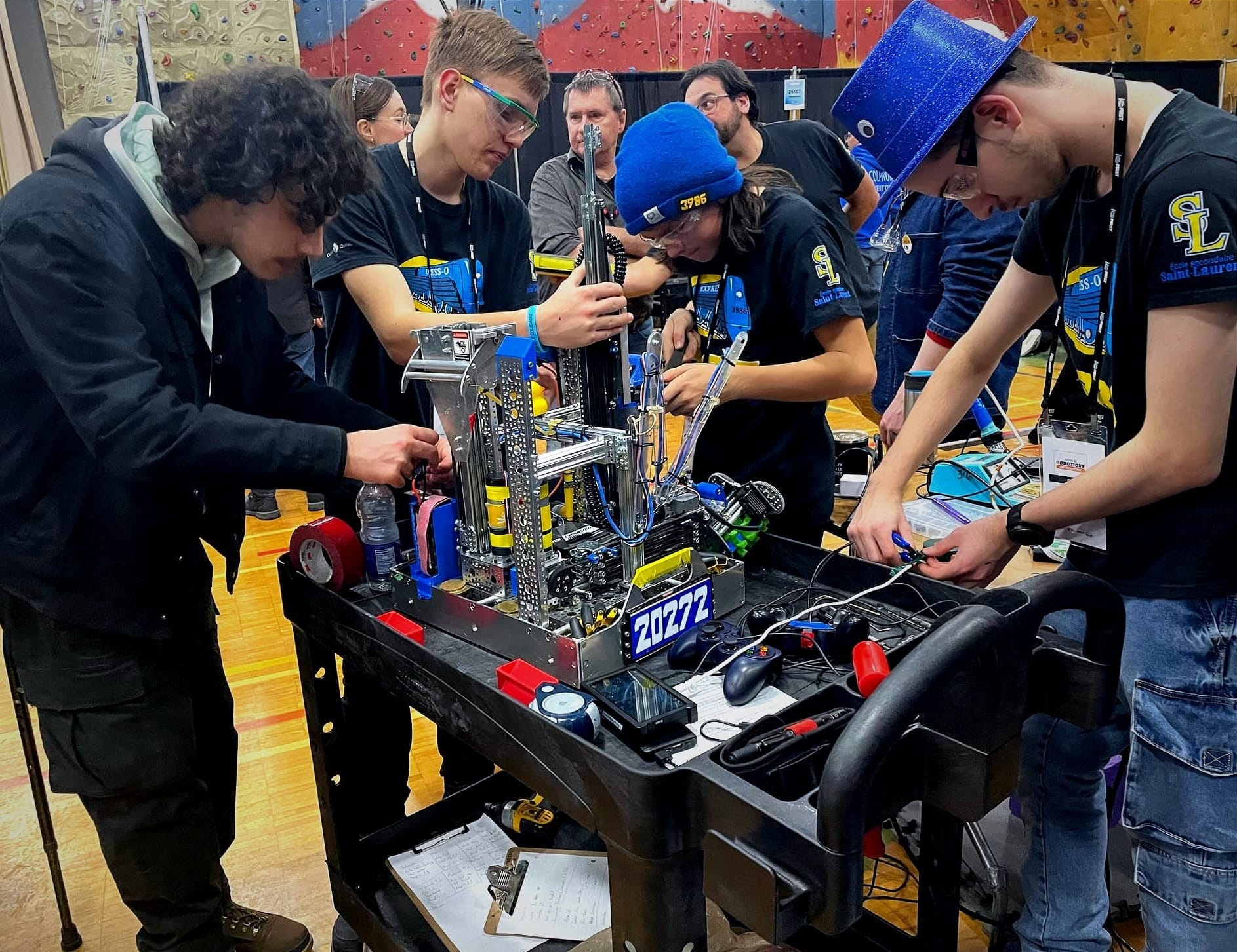 Quatre personnes autour d'un chariot, dans un gymnase, travaillant sur différentes pièces d'un robot. 