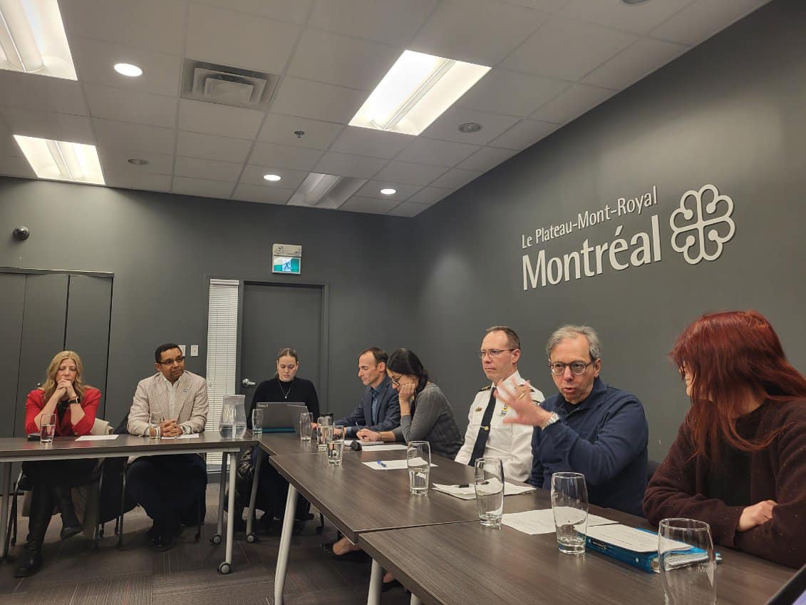 Huit personnes assises derrière des tables rectangulaires. 