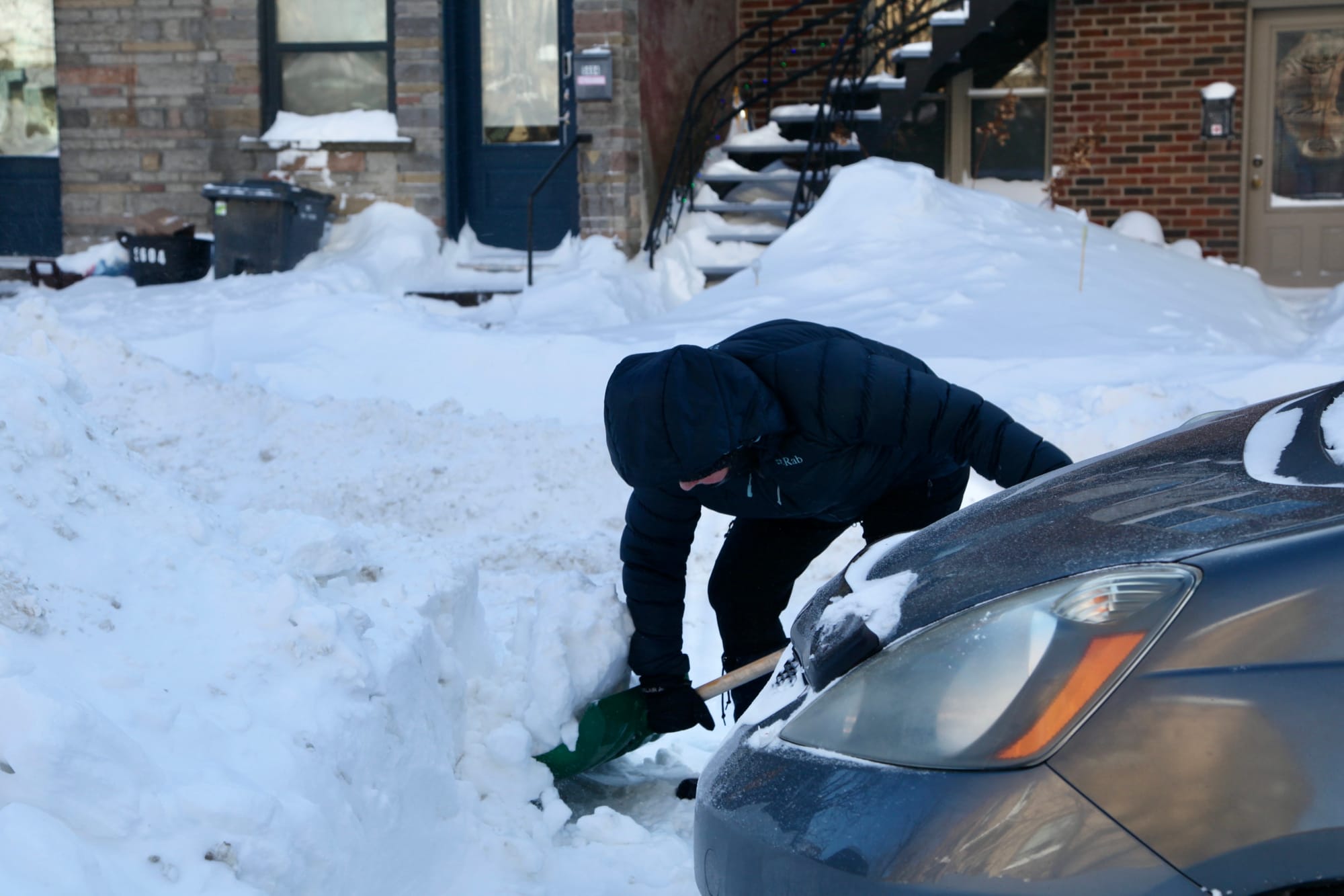 Une femme penchée ramasse une bonne portion de neige dans sa pelle.