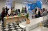 On y voit deux salles où discutent des gens et sont installées des tables avec nourriture et boisson.